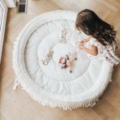 Child playing with toys on a round white mat in a room with wooden flooring.