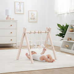 Baby lying on a white rug in a room with a wooden baby gym and white furniture.