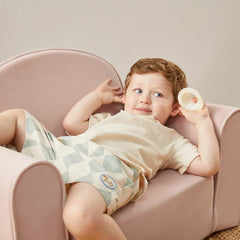 Child lying on a pink chair holding a bottle