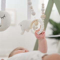 Baby hand reaching for a white baby mobile with hanging toys.