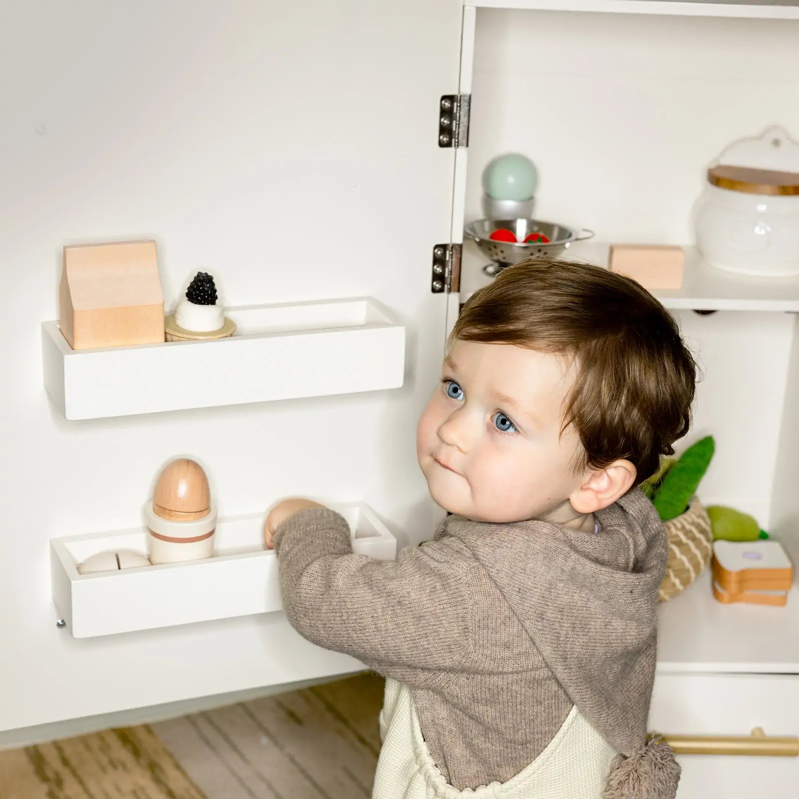 Child reaching into wooden play fridge