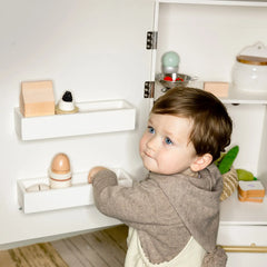 Child reaching into wooden play fridge