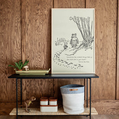 Framed illustration of a bear and a cat on a wooden wall above a black table with decorative items.