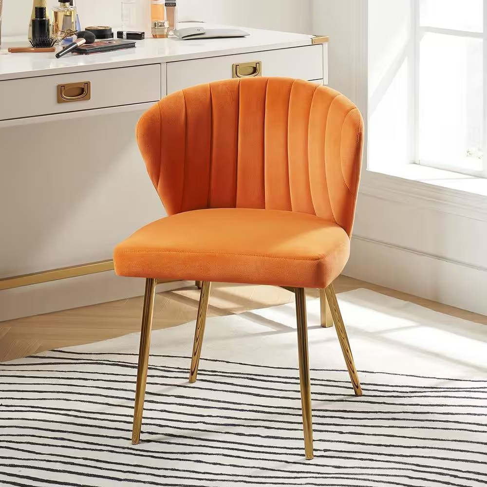 Orange velvet chair with gold legs in a room with a desk and window.