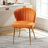 Orange velvet chair with gold legs in a room with a desk and window.