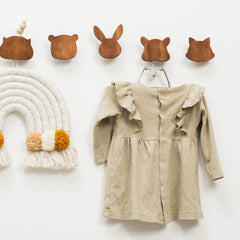 Beige dress hanging on a hook with wooden animal-shaped hooks and a macramé wall hanging on a white background