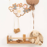 Wooden shelf with decorative items including a plush bunny, camera, and floral clock on a white wall.