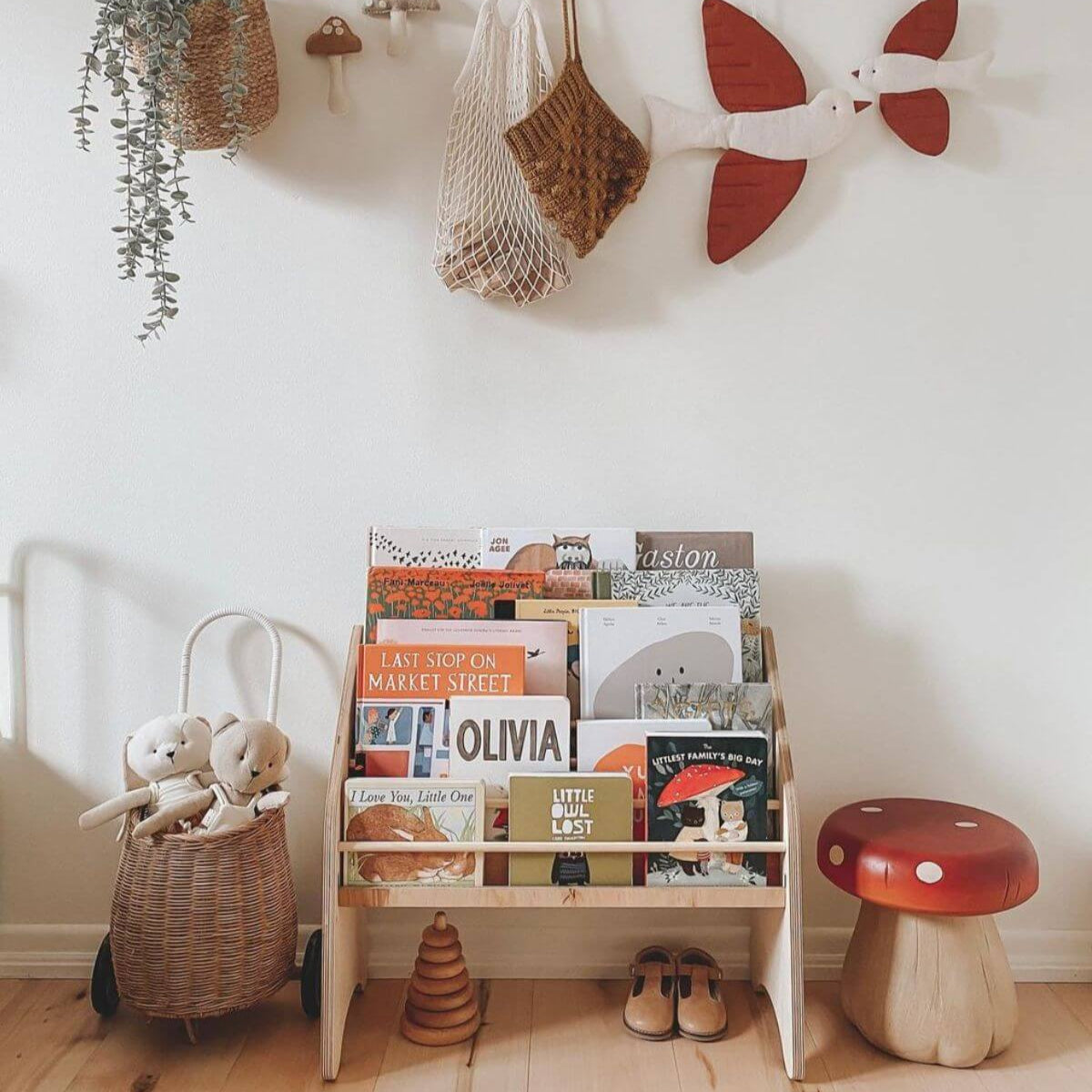 Children's bookshelf with books and toys in a room with a white wall and wooden floor.