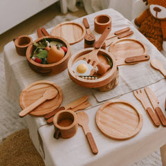 Wooden toy kitchen set on a tablecloth with a teddy bear in the background