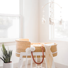 Nursery room with a wicker crib, white stool, and hanging mobile.