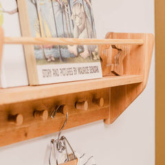 Wooden shelf with hooks holding a book and decorative items on a white wall.