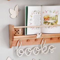Wooden shelf with books and decorative butterflies on a light gray wall.