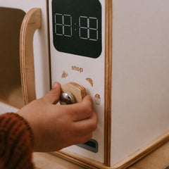 Hand pressing a button on a toy kitchen appliance with a digital display.