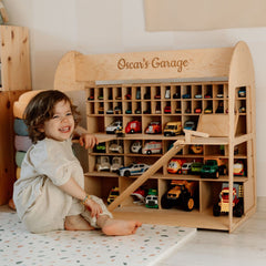 Child playing with a wooden toy garage filled with colorful model cars.
