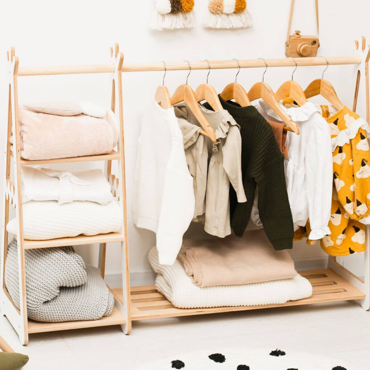 Wooden clothing rack with folded clothes and hangers on a white background