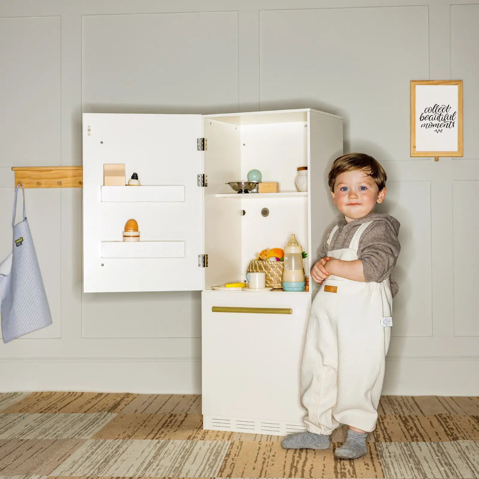 Child standing next to wooden play fridge