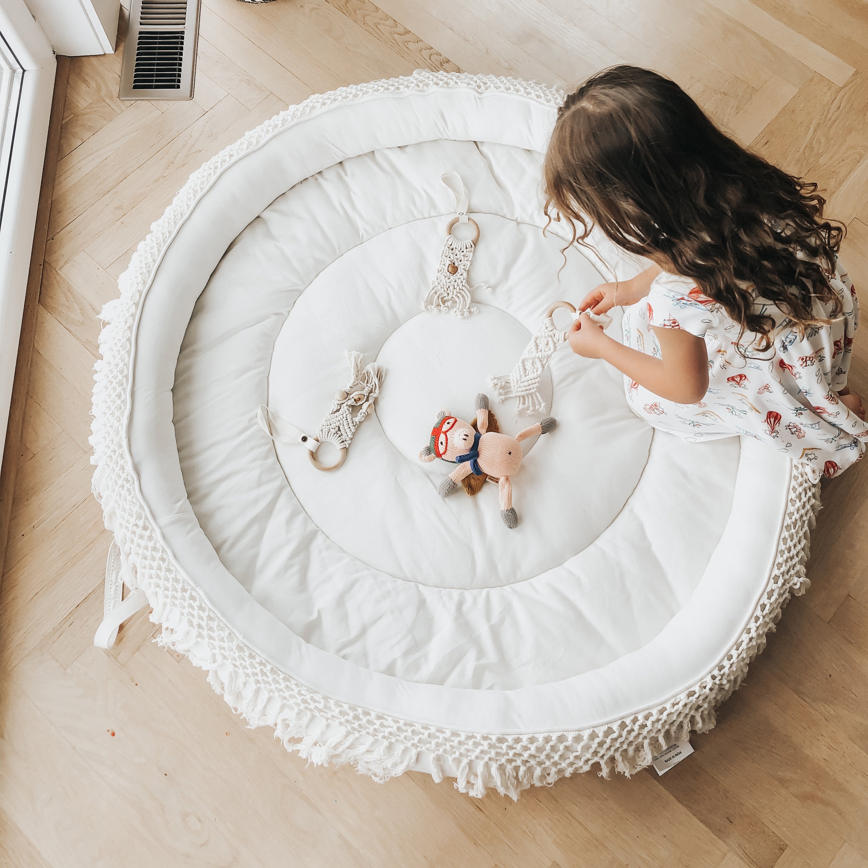 Child playing with toys on a round white mat in a room with wooden flooring.