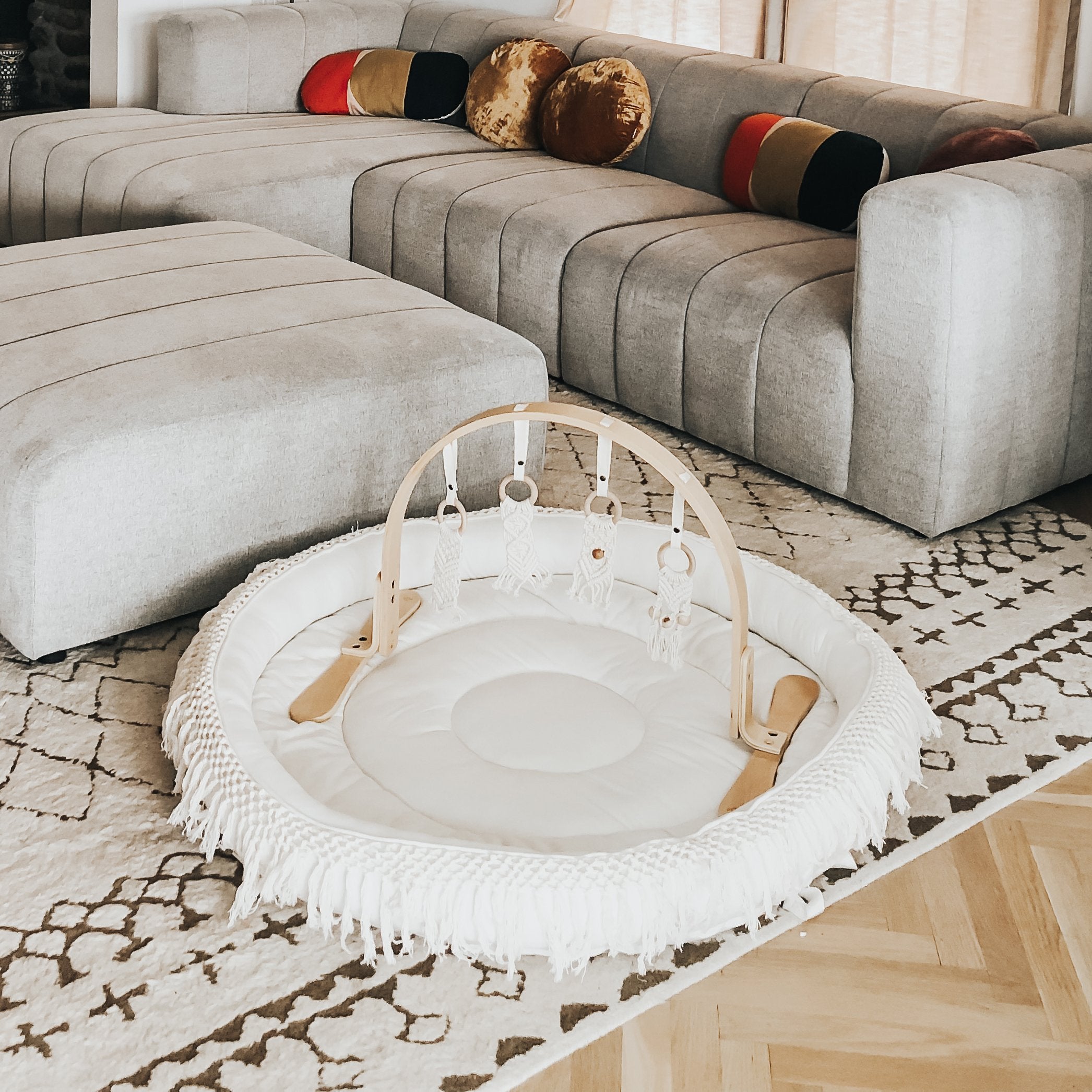 Gray sectional sofa with colorful cushions and a round white ottoman in a living room.