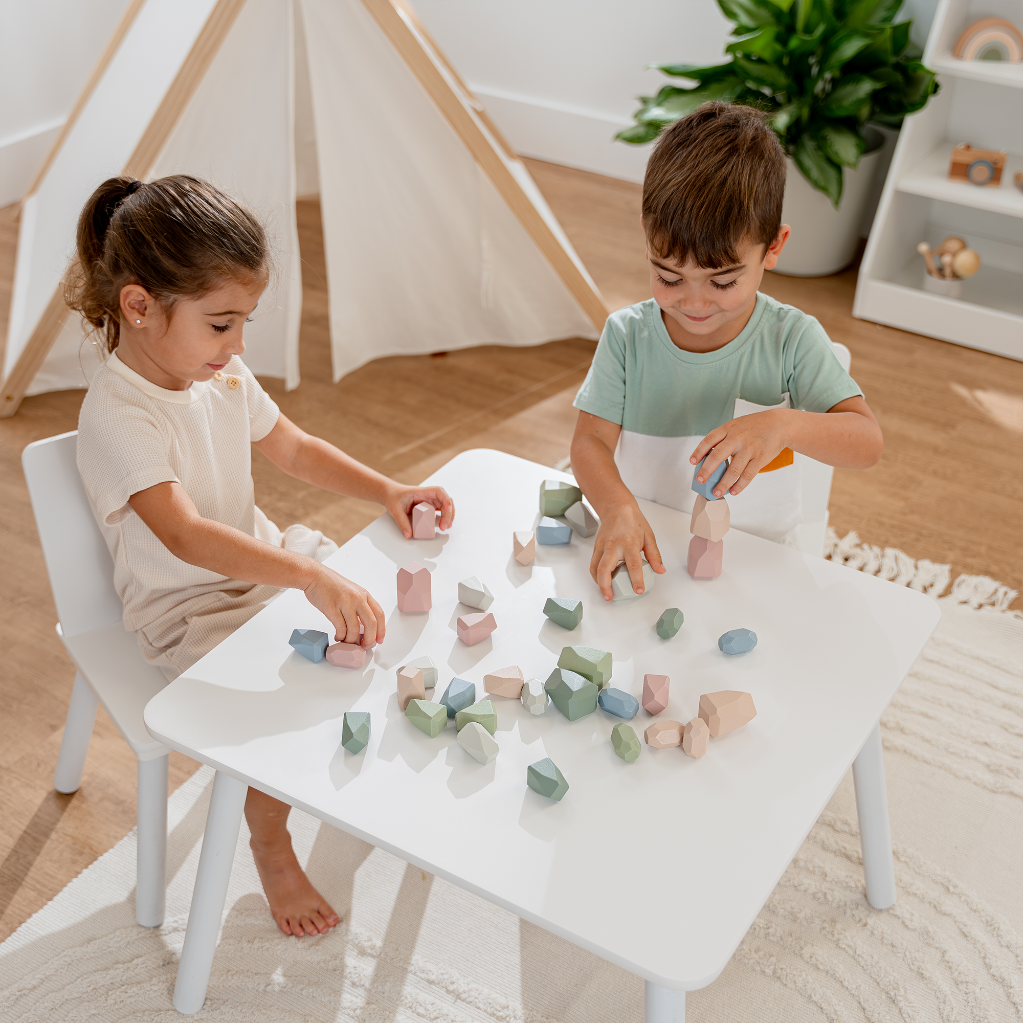 Two children playing with colorful wooden blocks at a white table in a cozy room.