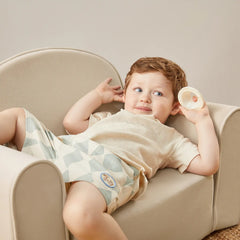 Child lying on a beige chair holding a small object