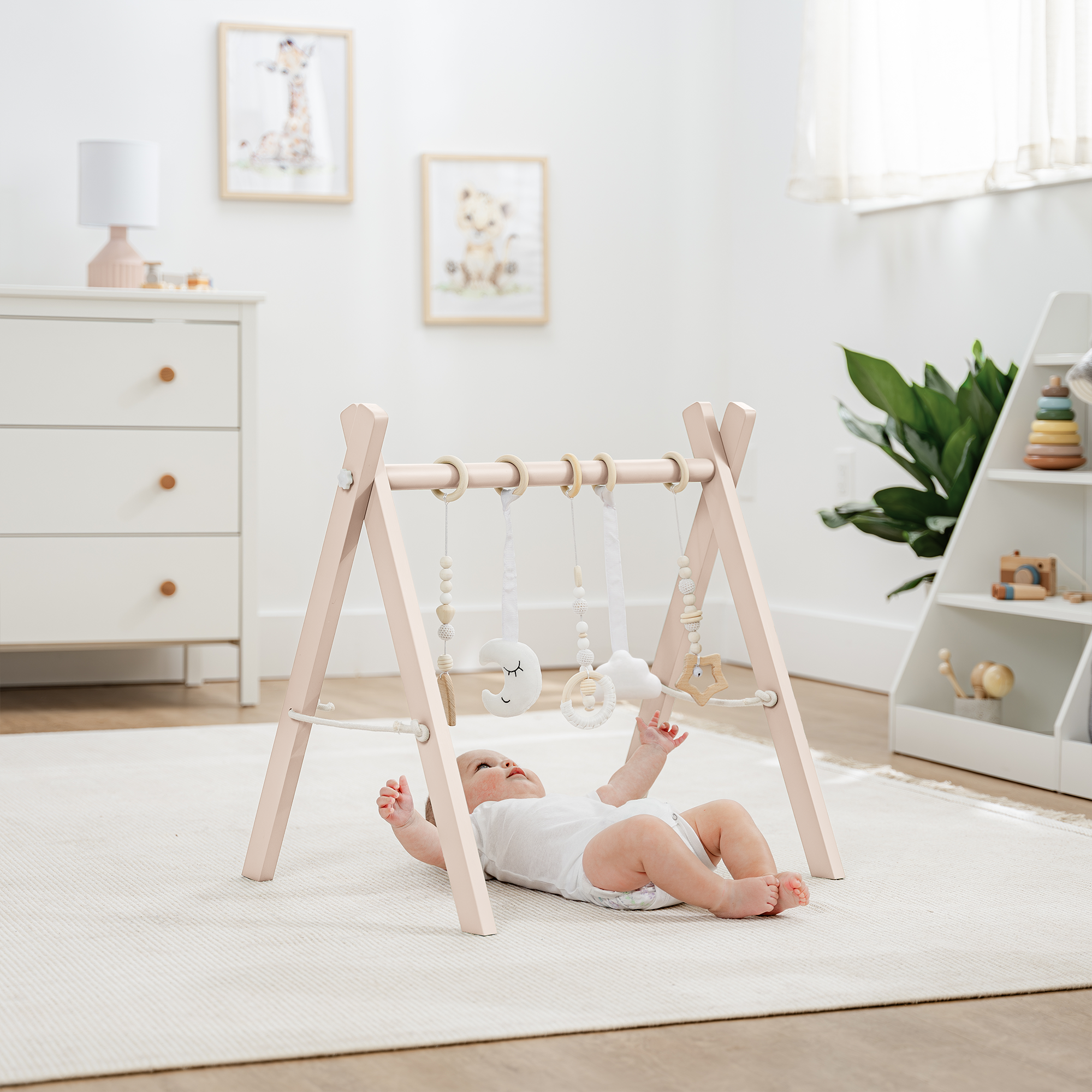 Baby lying on a white rug in a room with a wooden baby gym and white furniture.
