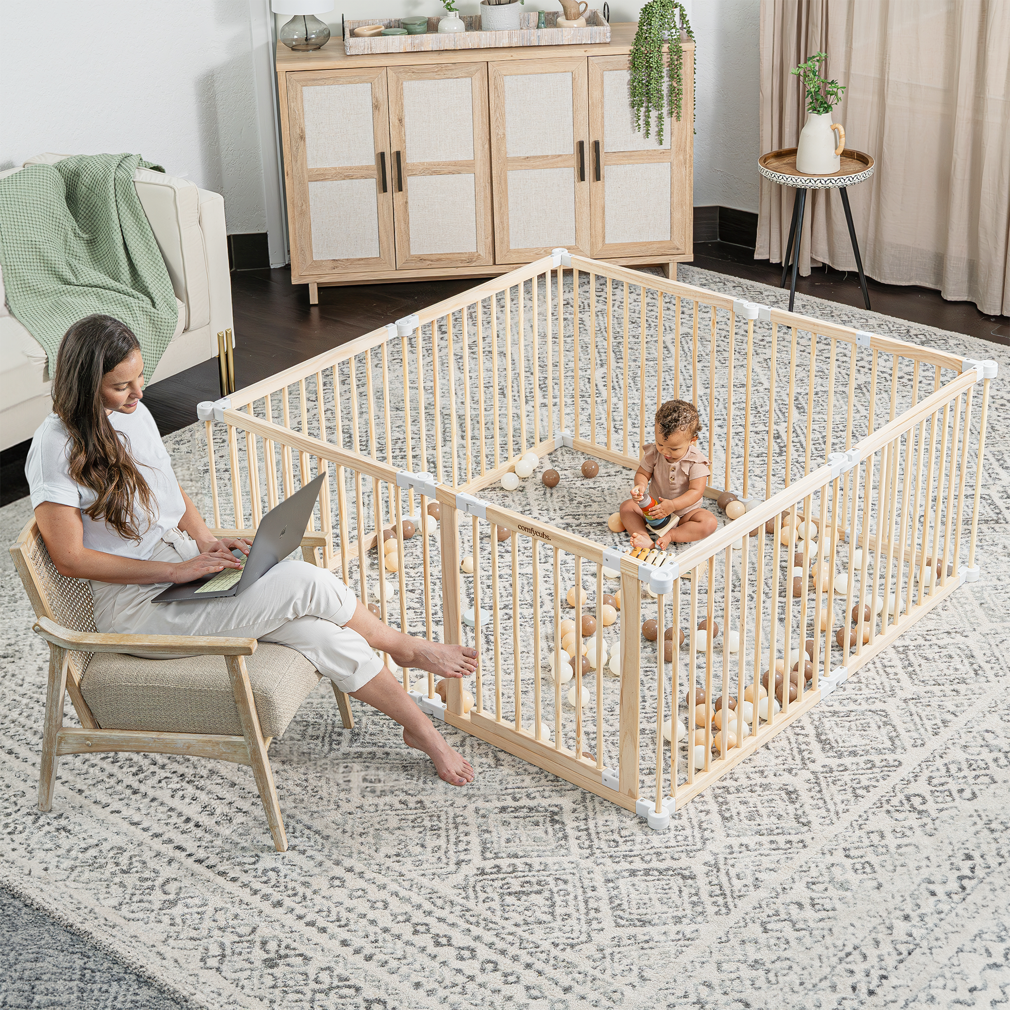 Mother placing baby inside natural wood toddler playpen in a modern family living space