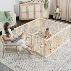 Mother placing baby inside natural wood toddler playpen in a modern family living space