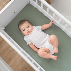 Baby lying in a crib with a green mattress cover