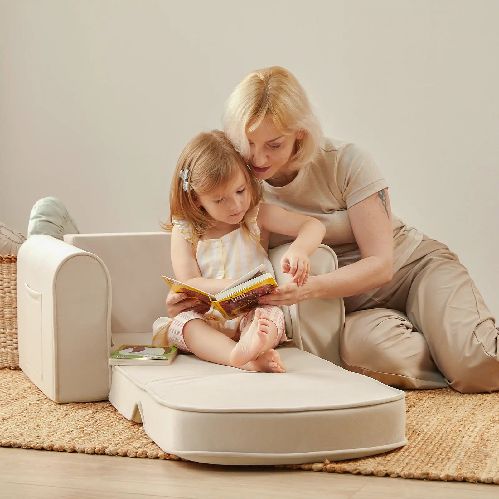Woman and child reading a book on a beige cushioned chair in a cozy room.