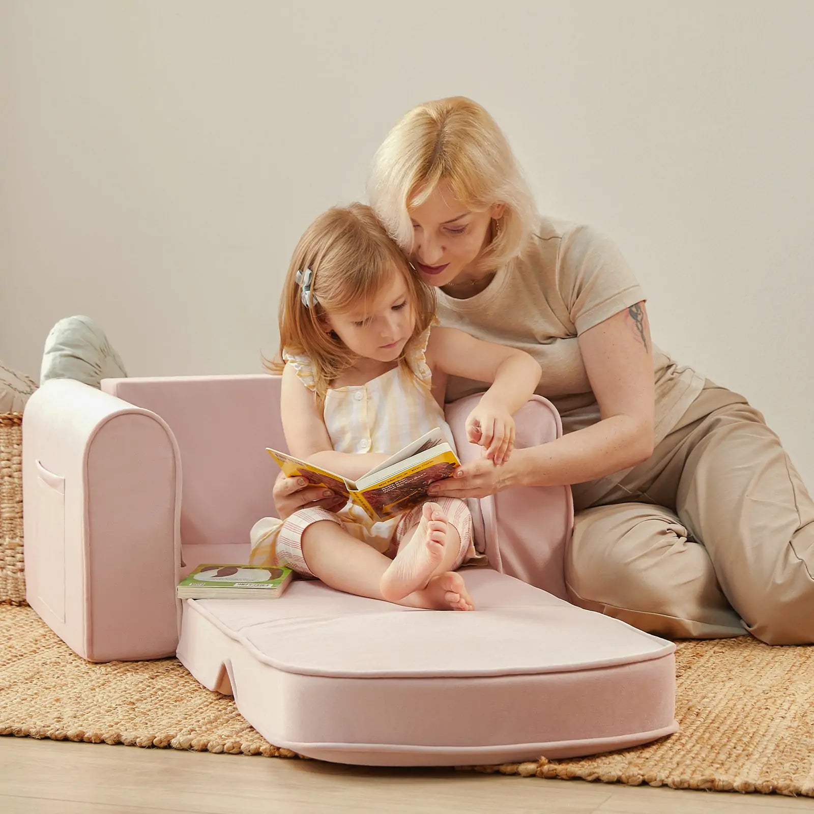 Woman and child reading a book on a pink children's sofa.