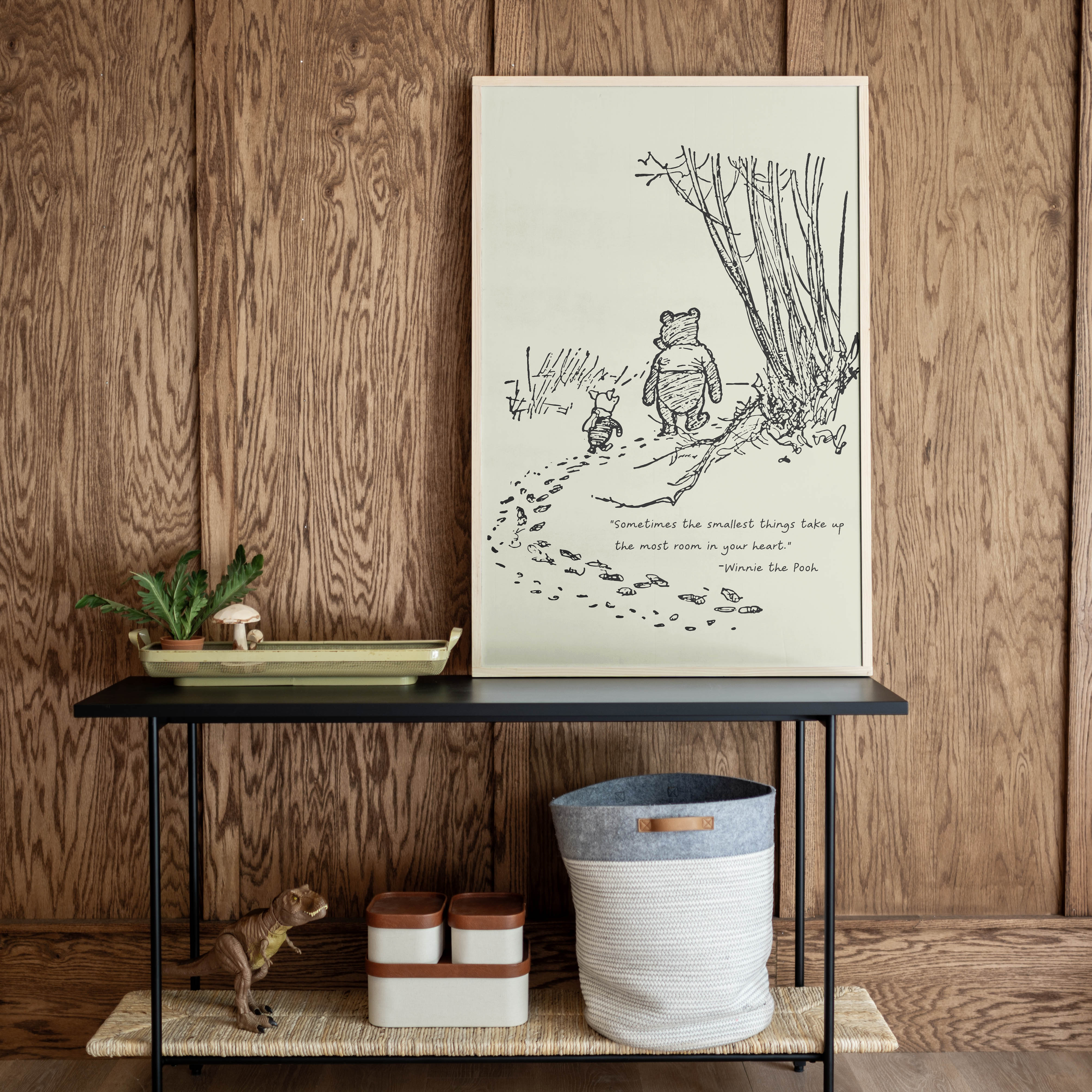 Framed illustration of a bear and a cat on a wooden wall above a black table with decorative items.