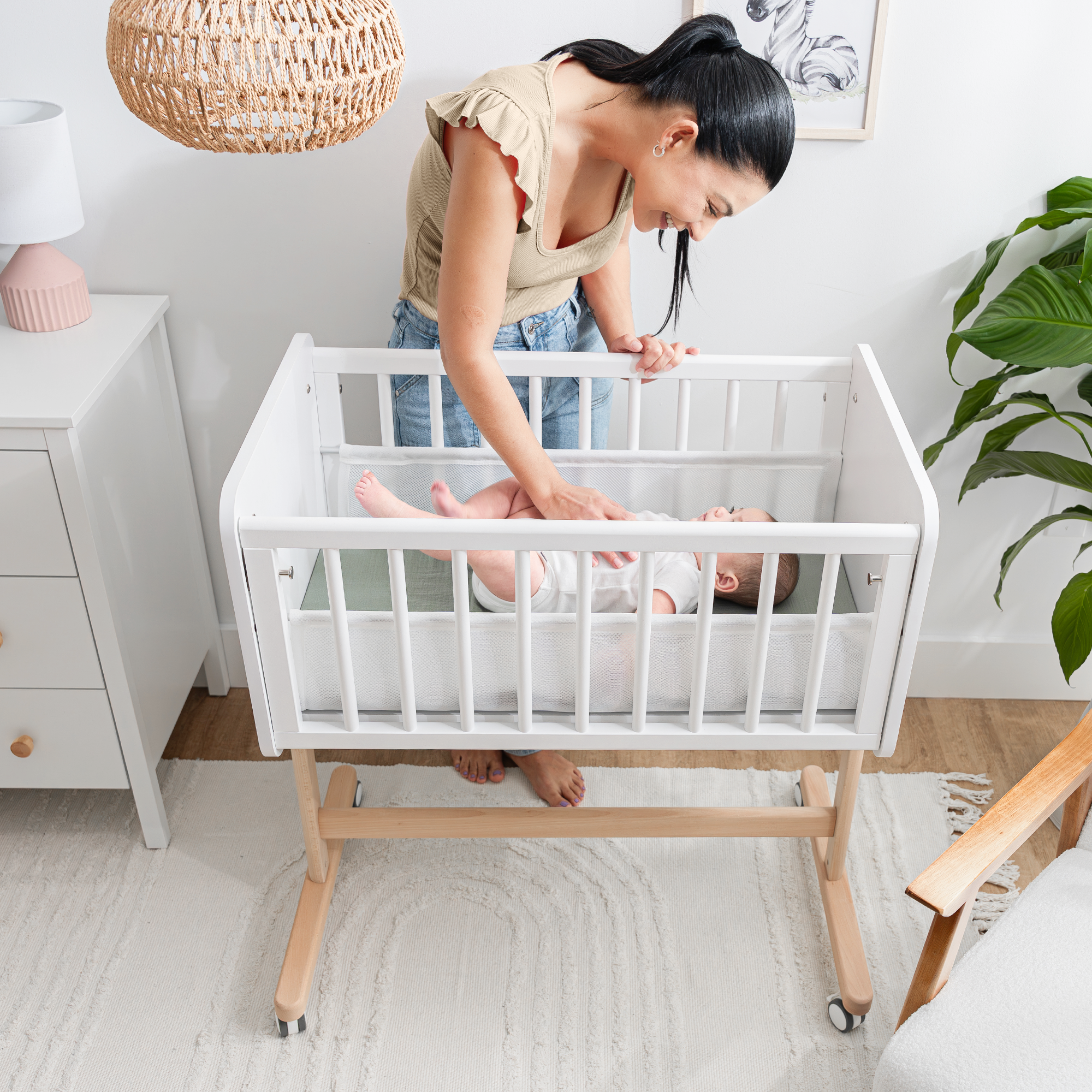 Woman adjusting a baby in a white crib in a nursery.
