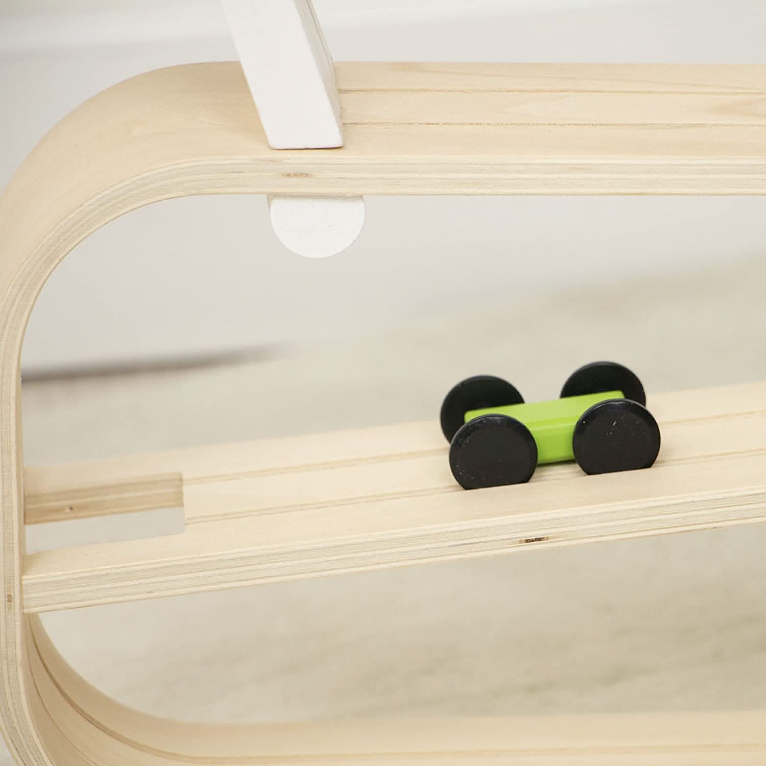 Small green toy car on a wooden shelf with a white background