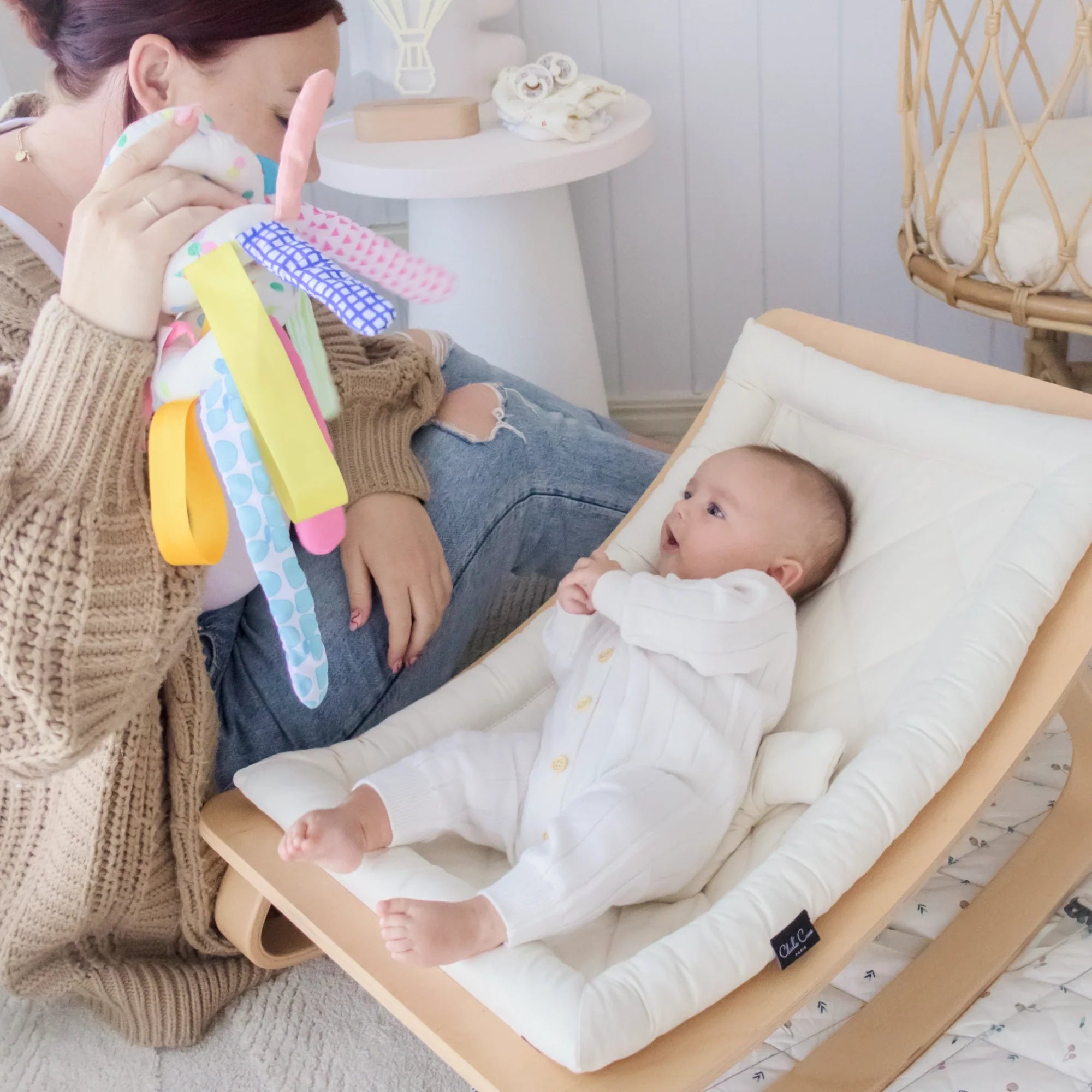 Baby laying on floor rocker with mom holding up toys