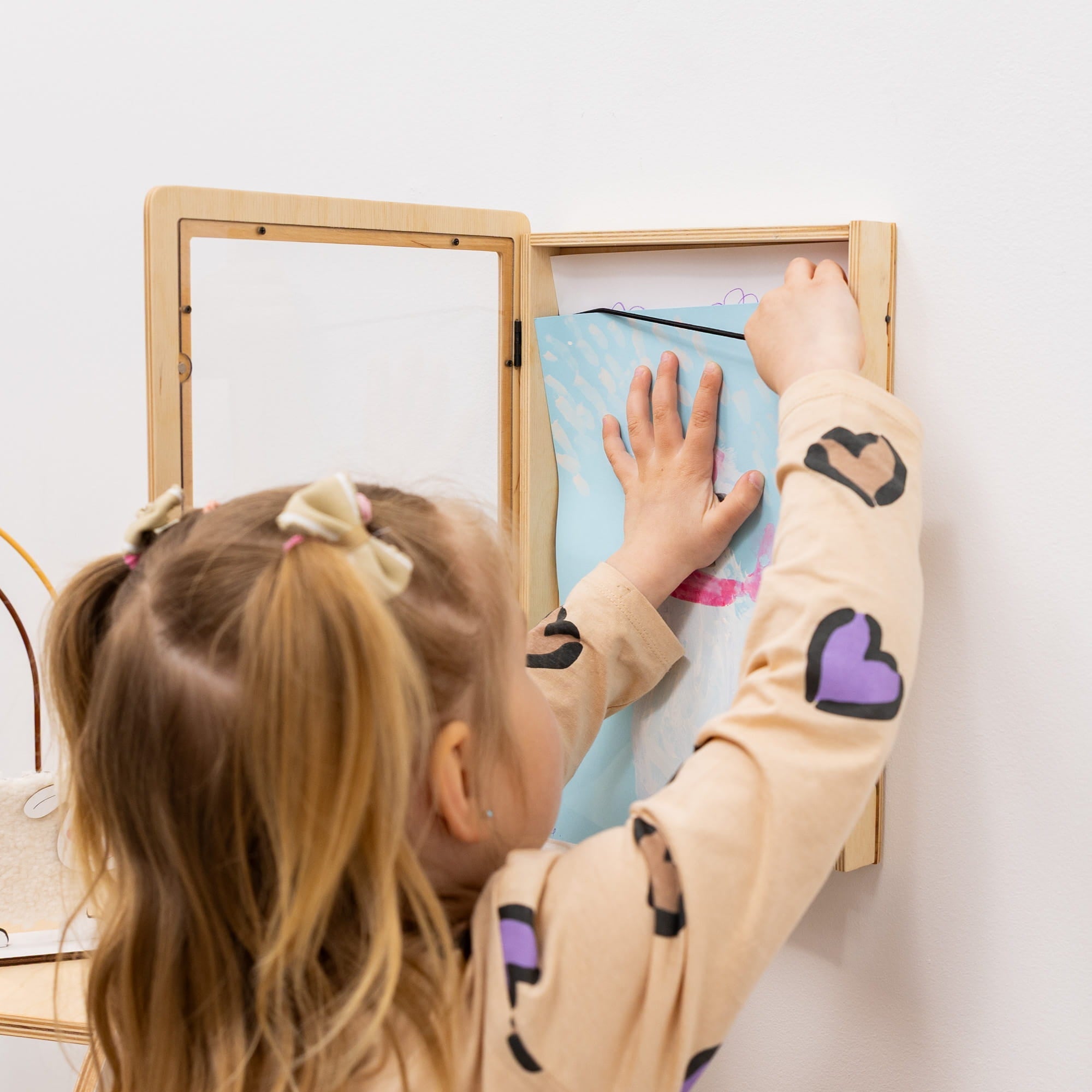 Child interacting with a wooden mirror on a white wall