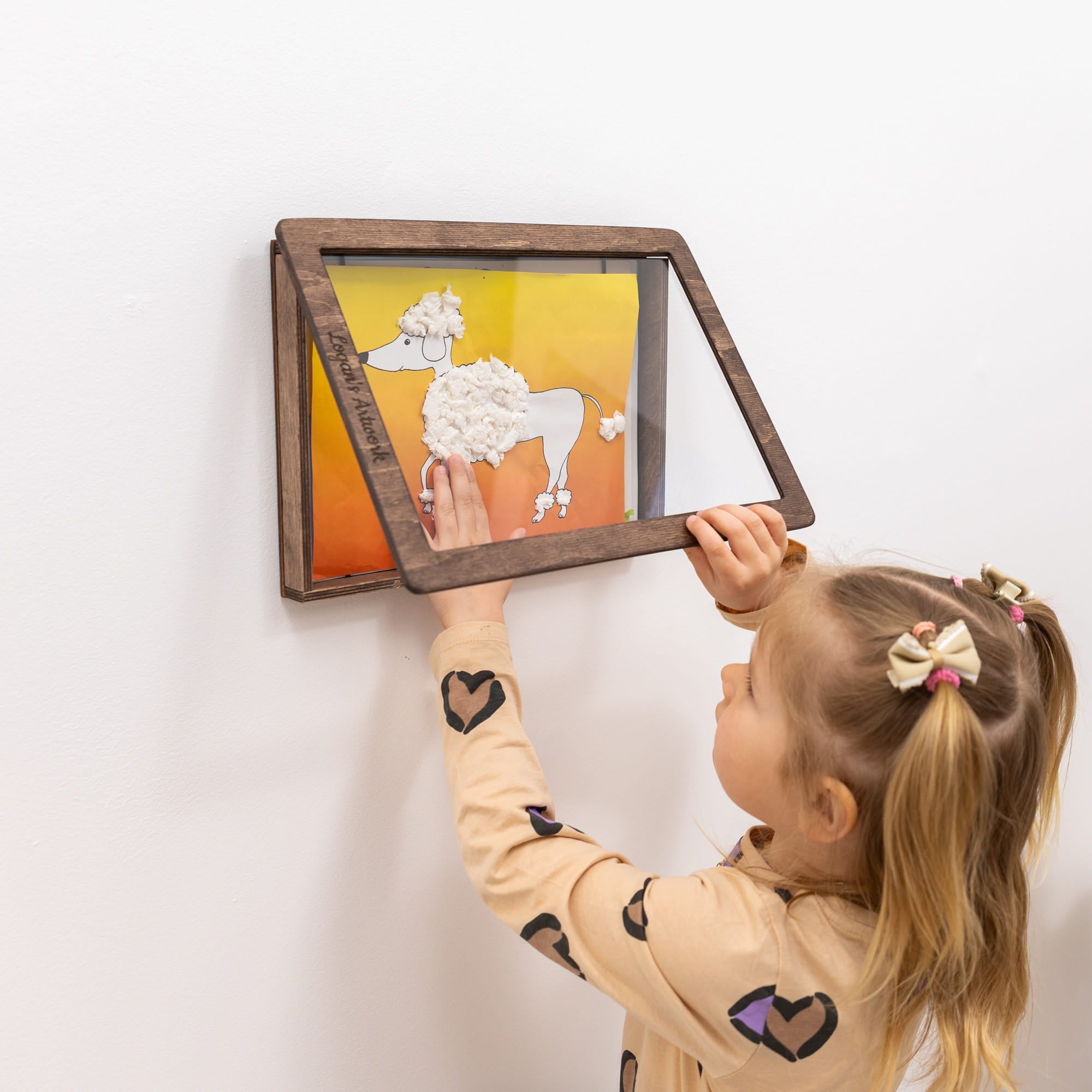 Child interacting with a framed shadow box art on a white wall