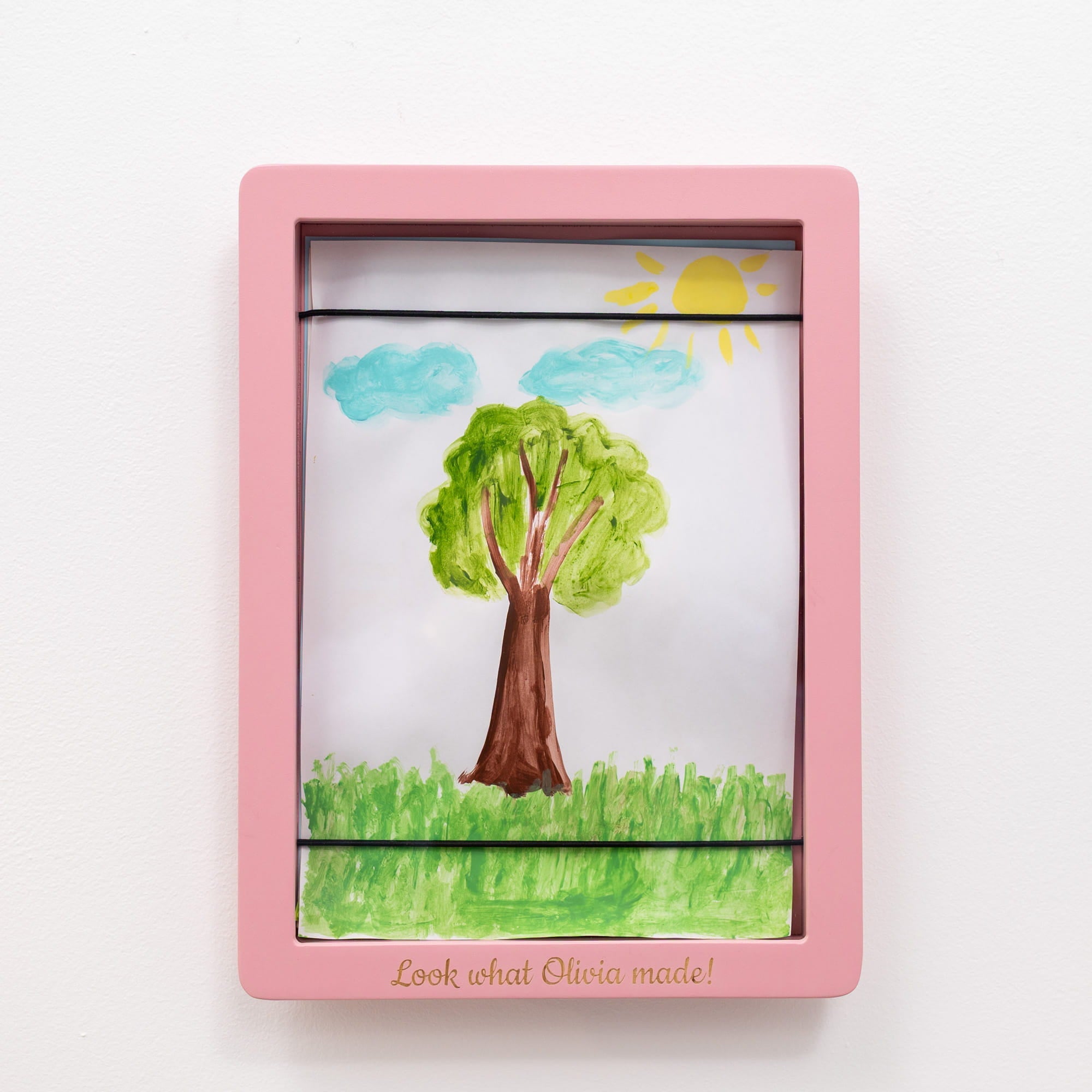 Pink frame with a child's drawing of a tree, sun, and clouds on a white background.