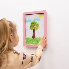 Child looking at a framed drawing of a tree with a sun and clouds on a white wall.