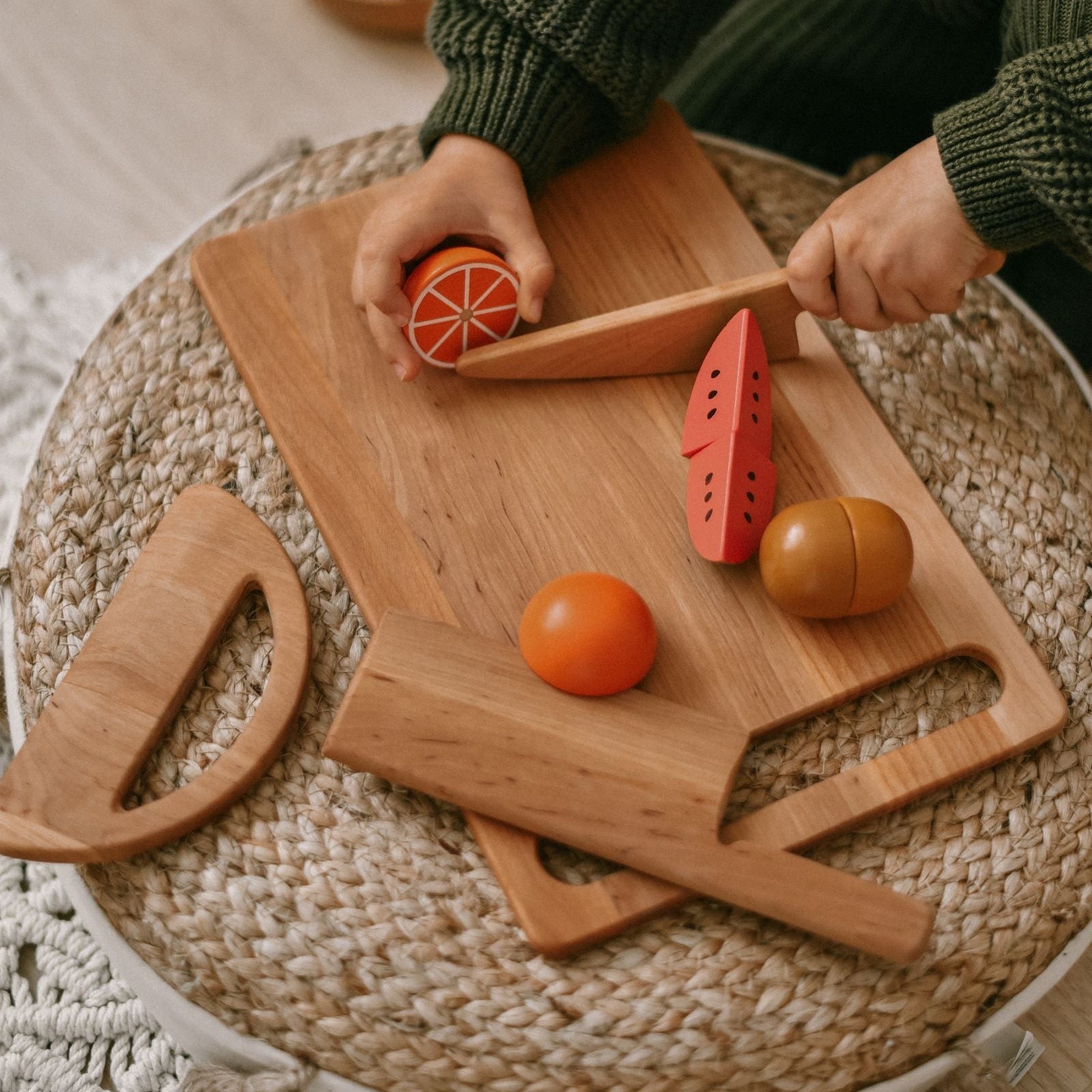 Person cutting an orange on a wooden cutting board with fruit-shaped cutters on a textured surface.