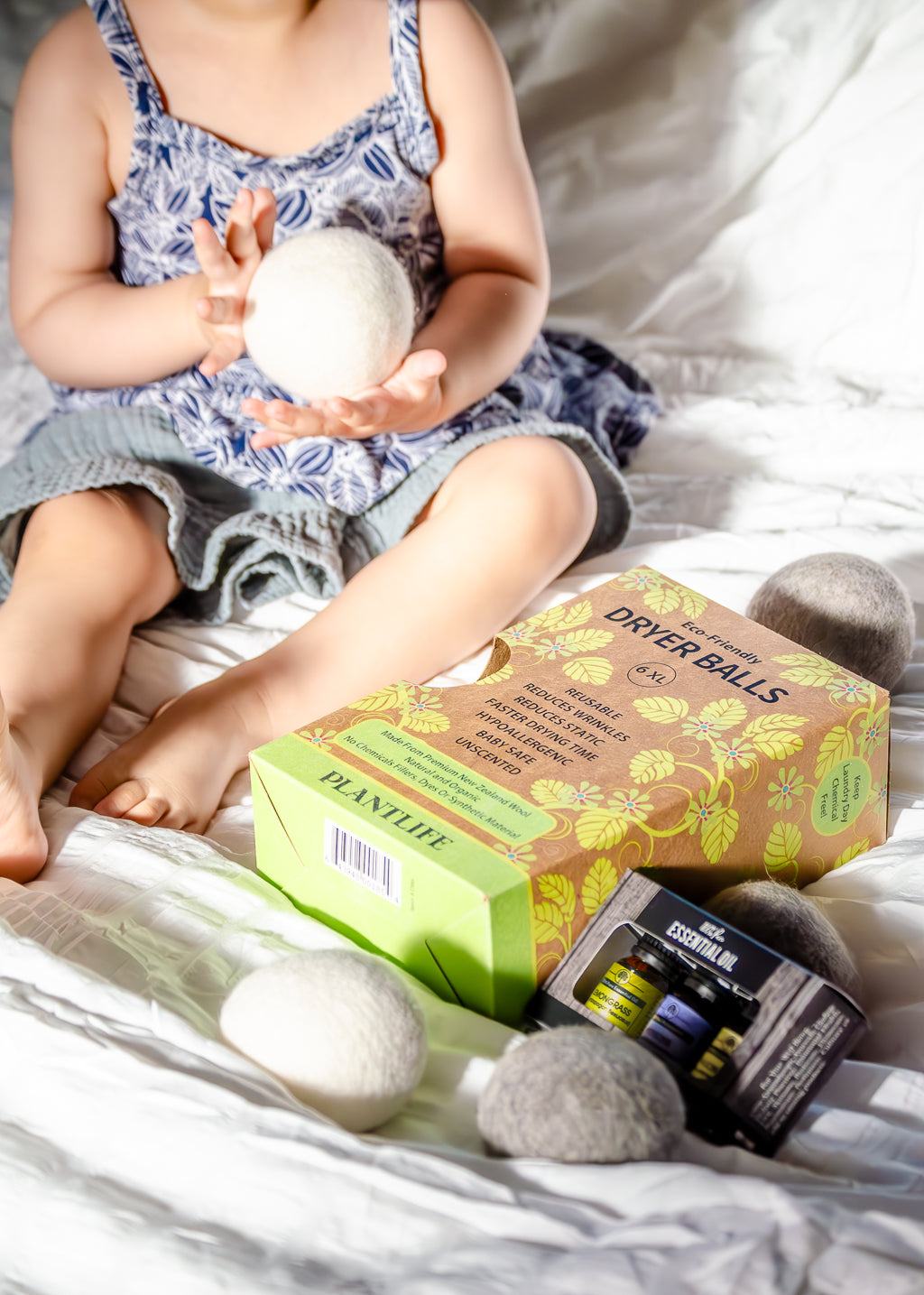 Child holding dryer balls with a box of dryer balls on a bed