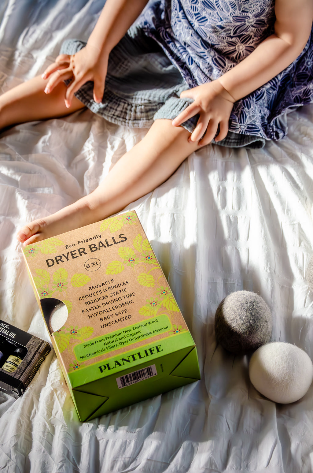 Box of Plantlife dryer balls on a bed with a person holding dryer balls.