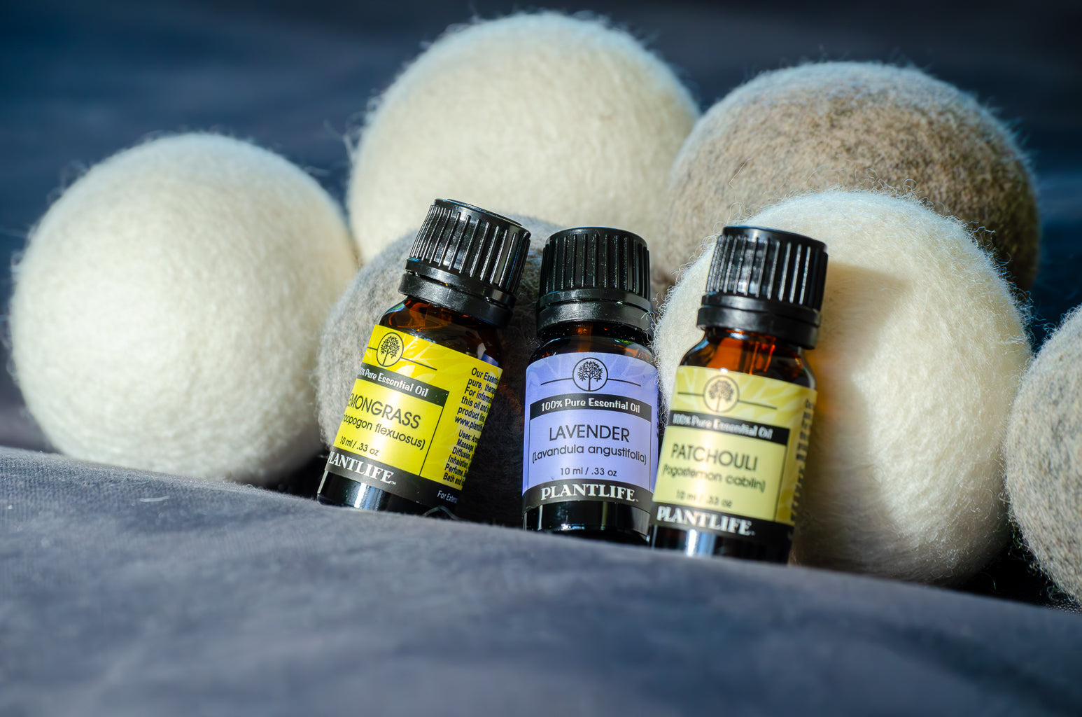 Three small bottles of Plantlife essential oils with wool dryer balls in the background.