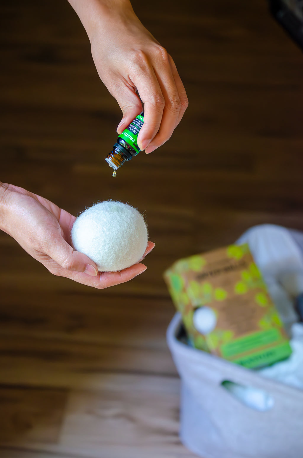 Person holding a white ball and a bottle of essential oil on a wooden floor.