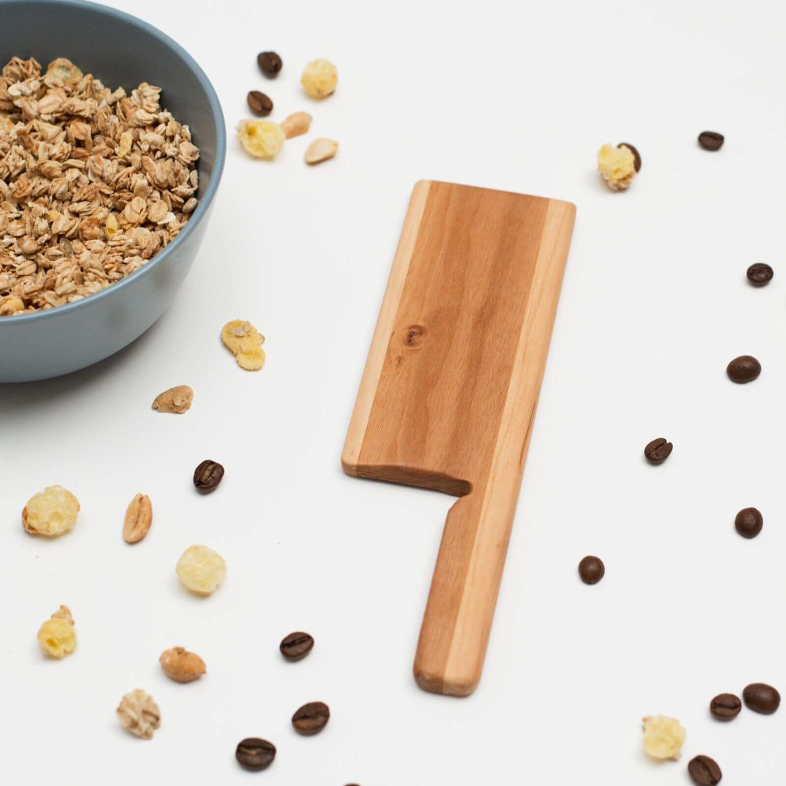 Wooden paddle on a white surface with granola, nuts, and coffee beans.