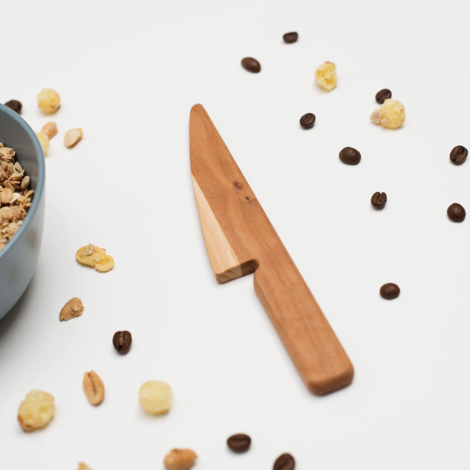 Wooden knife on a white surface with scattered nuts and seeds