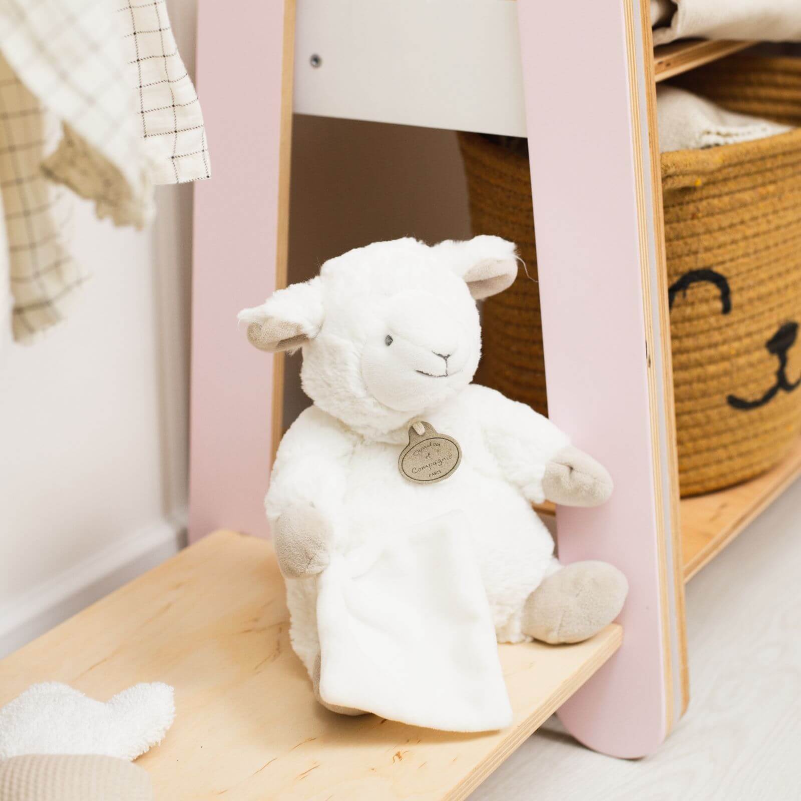 White plush lamb toy with a tag on a wooden shelf in a child's room.
