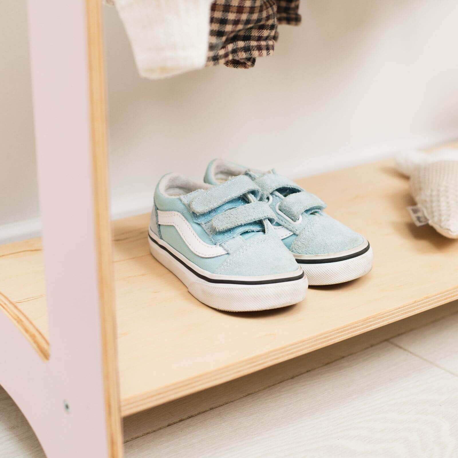 Pair of light blue children's sneakers on a wooden shelf.