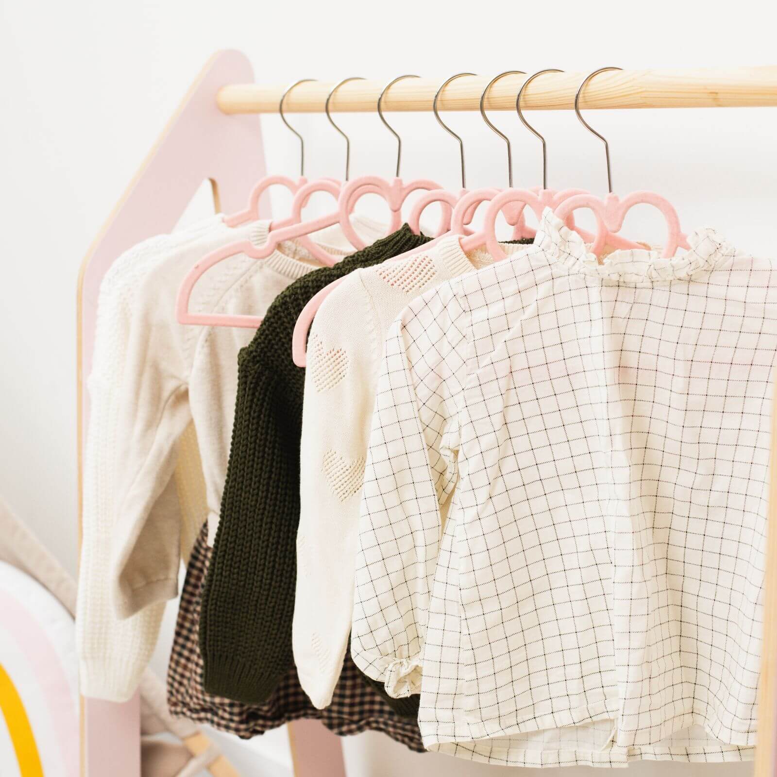 Clothing items on pink hangers on a wooden rack against a light background