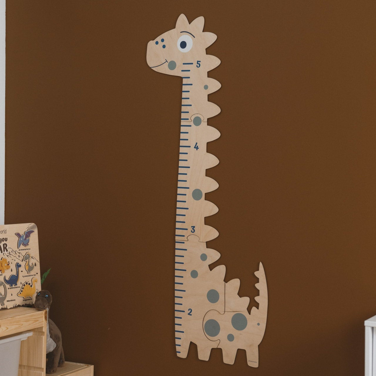 Dinosaur-shaped growth chart on a brown wall with children's books and toys below.