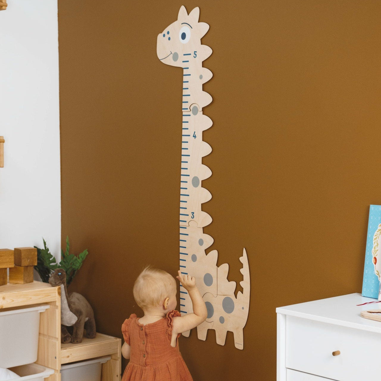 Child reaching up to a dinosaur-shaped growth chart on a brown wall.